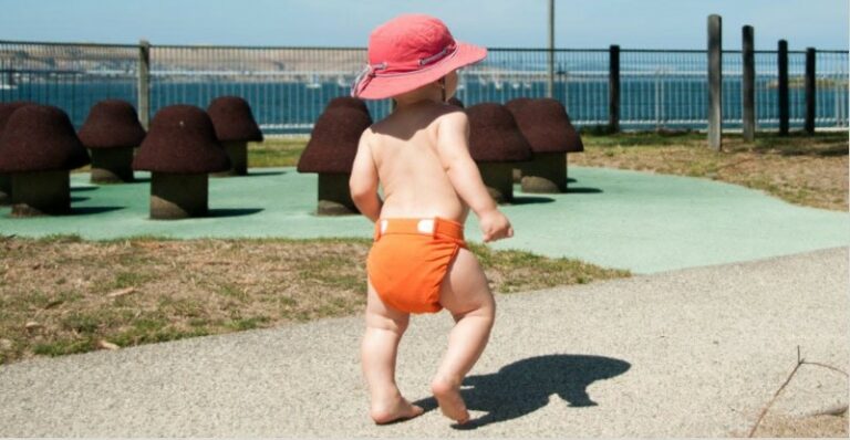 Best compostable nappies in Australia-Bab walking confidently with an orange Eenee nappy and wearing a sunhat.