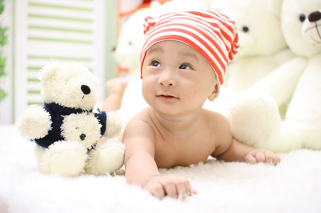 What are the Best organic stuffed animals for babies?-Baby laying on belly beside stuffed white bear toy.