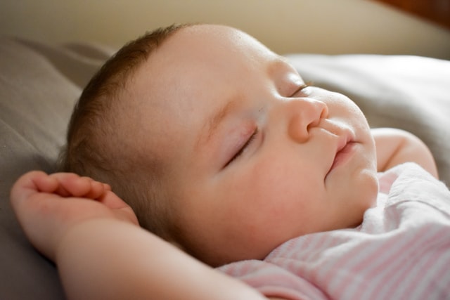 Sleeping baby wearing pinks white striped outfit.