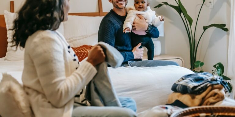 Hanna Andersson VS Primary-Family sitting on a double bed with baby sorting out baby clothes.