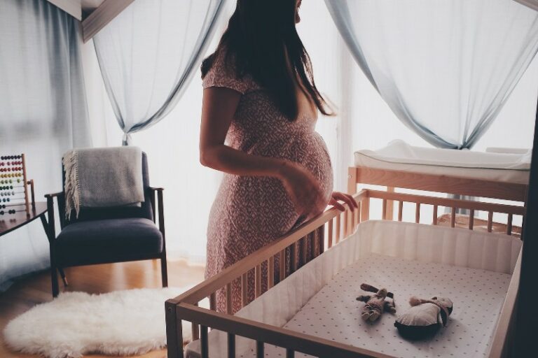 What is Hire for baby?- Pregnant lady standing in baby nursery looking at a full sized crib.