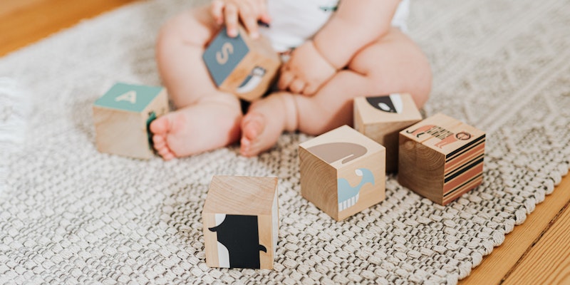What is Aster and Oak?- baby sitting on the floor playing with wooden blocks.
